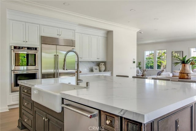 kitchen featuring stainless steel appliances, light stone countertops, white cabinetry, and a sink
