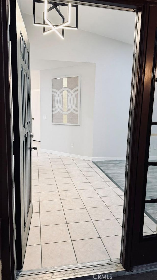 hall with baseboards, vaulted ceiling, and light tile patterned flooring