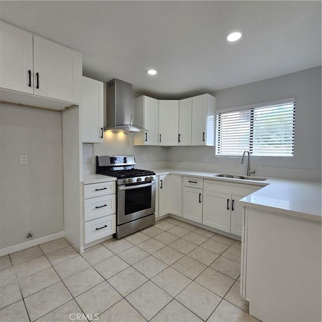 kitchen with stainless steel gas range, wall chimney range hood, light countertops, white cabinetry, and a sink