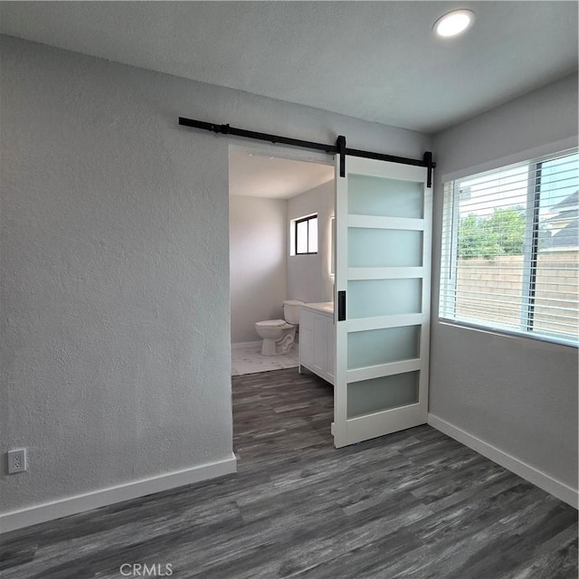 interior space featuring baseboards, a textured wall, a barn door, and dark wood-type flooring