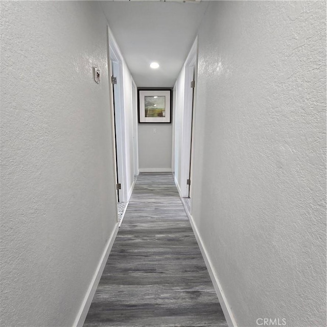 corridor with a textured wall, baseboards, and dark wood-type flooring