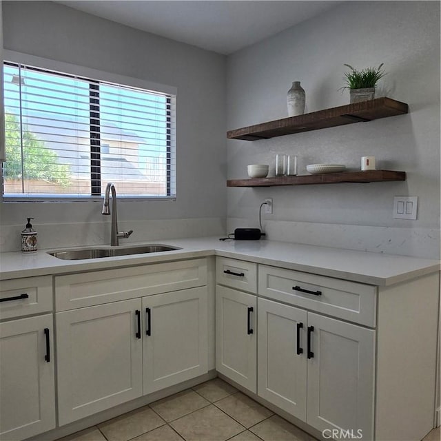 kitchen featuring open shelves, light tile patterned flooring, light countertops, white cabinets, and a sink
