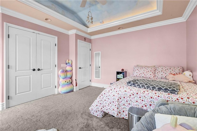 carpeted bedroom featuring ceiling fan, a raised ceiling, baseboards, ornamental molding, and a closet