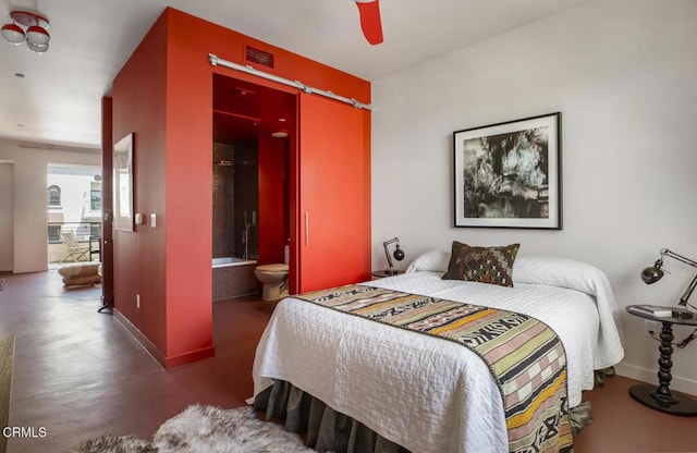 bedroom featuring concrete flooring, baseboards, a barn door, and ensuite bath
