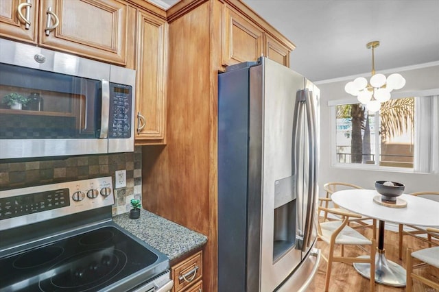 kitchen featuring crown molding, decorative backsplash, brown cabinets, a notable chandelier, and stainless steel appliances