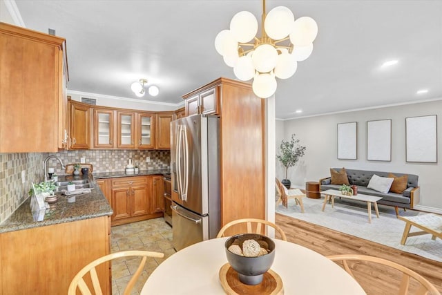 kitchen with brown cabinetry, backsplash, appliances with stainless steel finishes, a sink, and glass insert cabinets