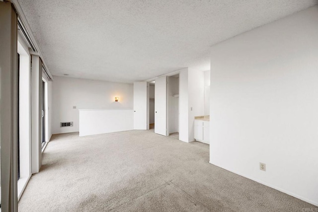 unfurnished living room featuring visible vents, a textured ceiling, and light carpet