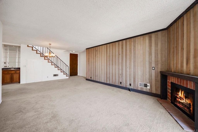 unfurnished living room featuring a brick fireplace, a textured ceiling, carpet, visible vents, and stairway