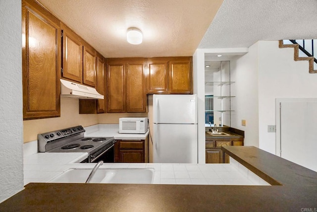 kitchen with white appliances, a textured ceiling, under cabinet range hood, brown cabinets, and a sink