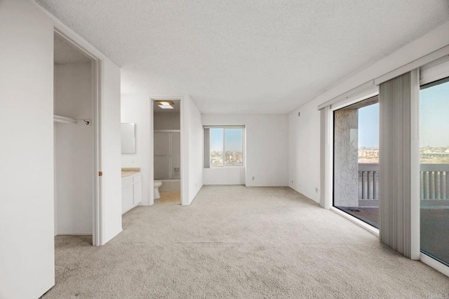 unfurnished bedroom featuring access to outside, ensuite bath, a textured ceiling, and light colored carpet