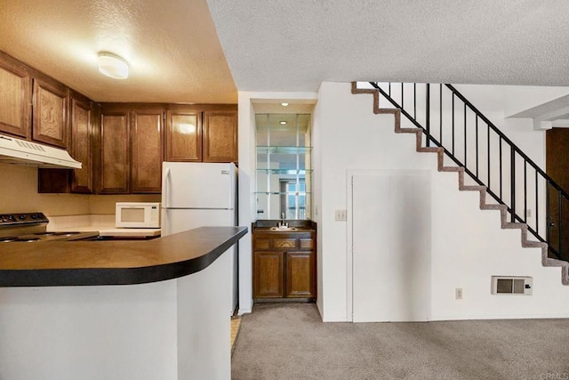 kitchen featuring a textured ceiling, light colored carpet, dark countertops, under cabinet range hood, and white appliances