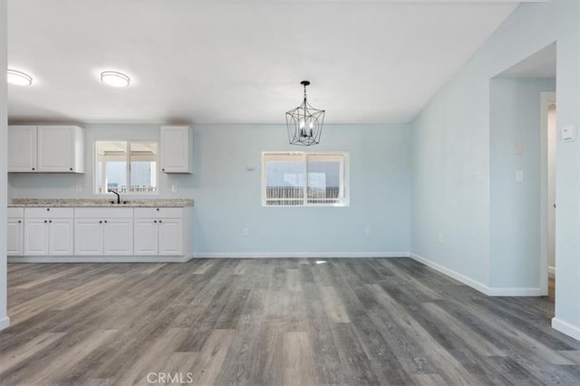 unfurnished dining area with baseboards, a sink, wood finished floors, and a chandelier