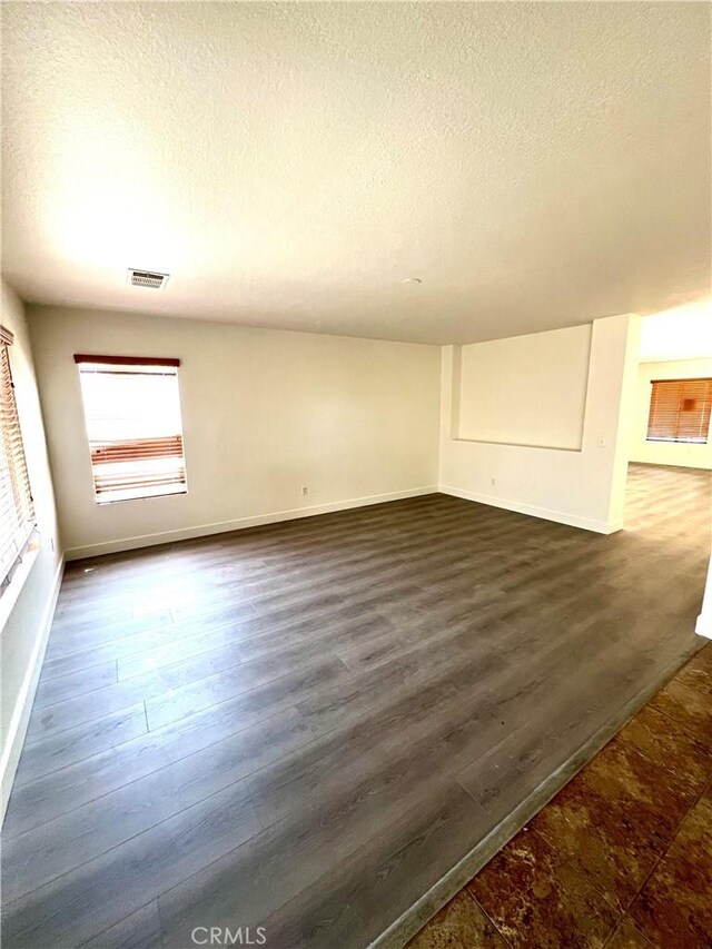 interior space with baseboards, dark wood-style floors, a textured ceiling, and visible vents