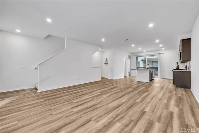 unfurnished living room with baseboards, recessed lighting, and light wood-style flooring
