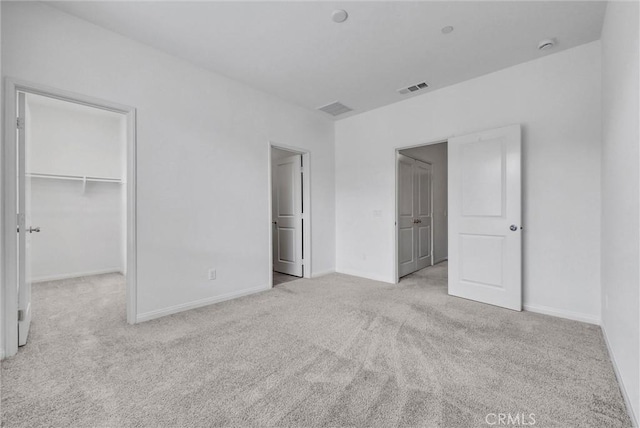 unfurnished bedroom with visible vents, a closet, baseboards, a walk in closet, and carpet flooring
