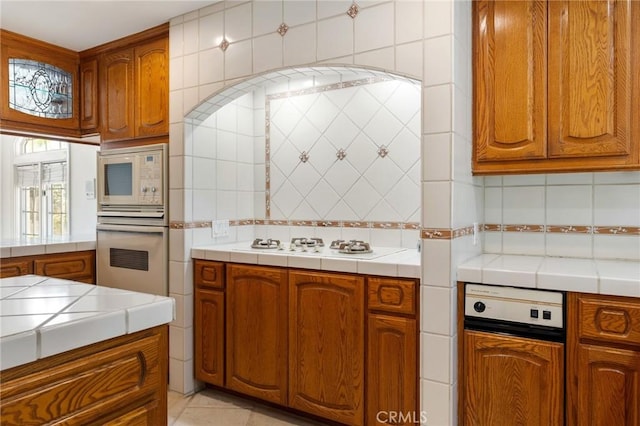 10703 Wheatland Ave, Sunland, CA 91040 - kitchen featuring white appliances, tile countertops, brown cabinetry, and decorative backsplash