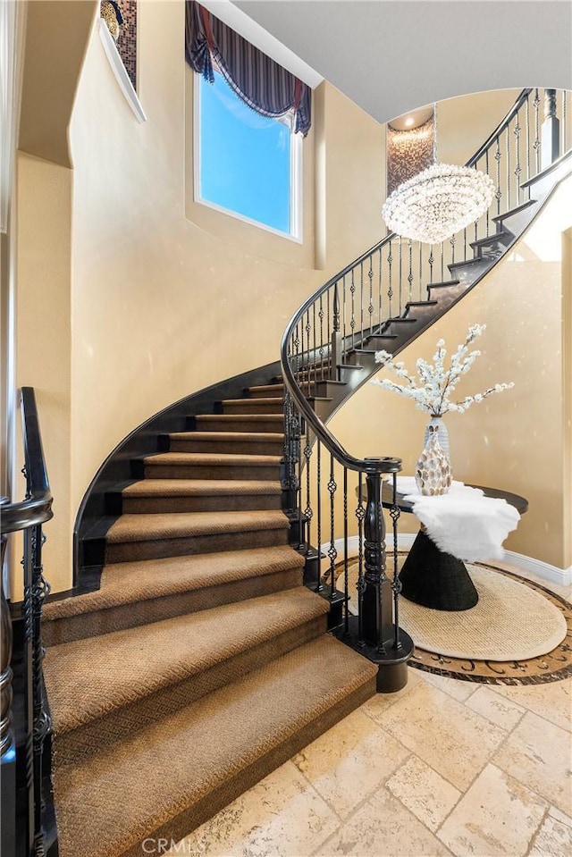 staircase with a towering ceiling, baseboards, and stone tile flooring