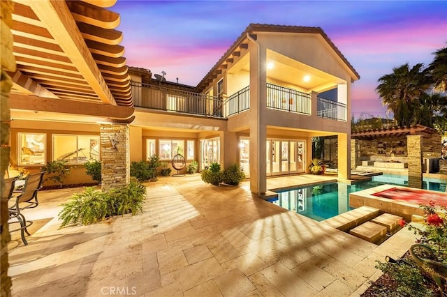 back of property at dusk featuring french doors, an outdoor pool, a patio area, a hot tub, and a balcony
