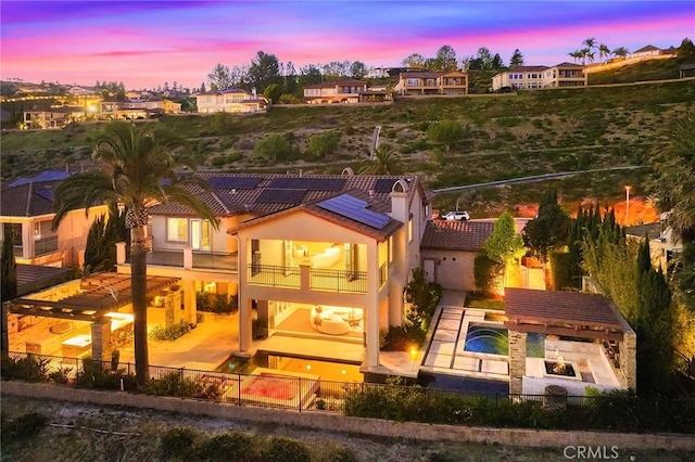 rear view of house featuring a hot tub, roof mounted solar panels, a fenced in pool, a fenced backyard, and a balcony