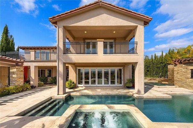 back of house featuring an in ground hot tub, a balcony, a patio area, and stucco siding