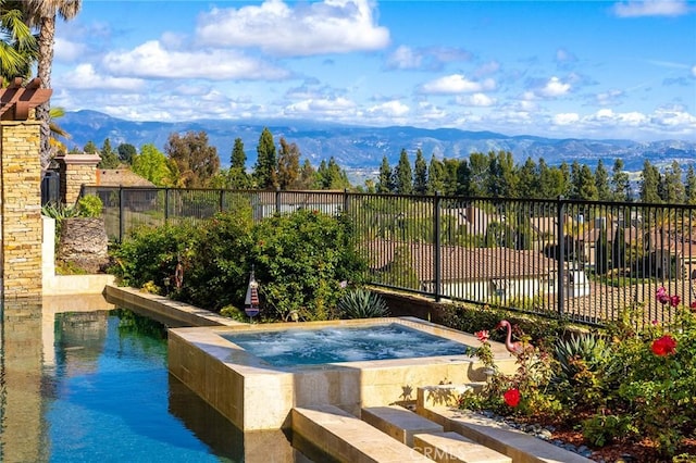 view of pool featuring fence, a swimming pool, a mountain view, and an in ground hot tub