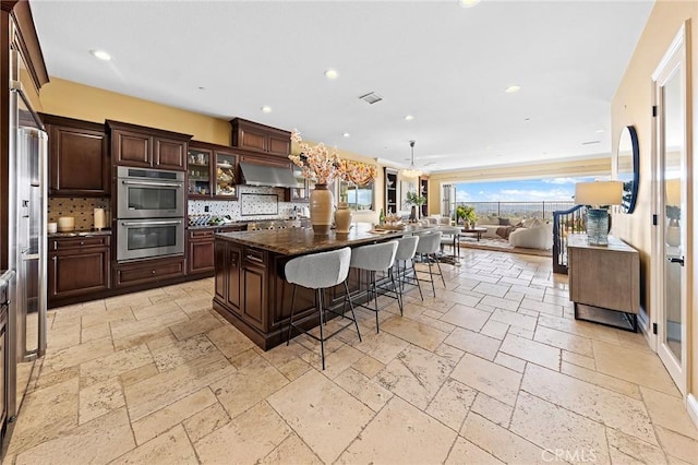 kitchen featuring double oven, stone tile floors, a kitchen breakfast bar, and tasteful backsplash