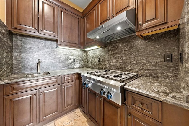 kitchen featuring a sink, dark stone counters, stainless steel gas stovetop, tasteful backsplash, and under cabinet range hood