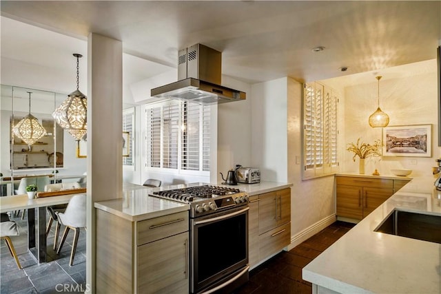 kitchen featuring baseboards, modern cabinets, wall chimney range hood, gas range, and hanging light fixtures