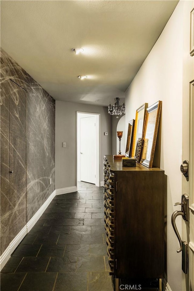 interior space with baseboards, a chandelier, stone finish floor, and an accent wall