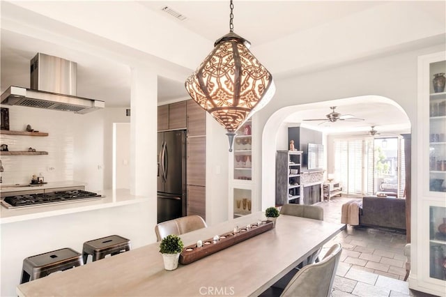 dining room with arched walkways, ceiling fan, stone tile floors, and visible vents