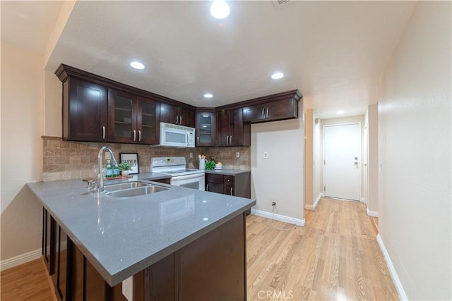 kitchen with a peninsula, dark brown cabinetry, white appliances, light wood-style floors, and a sink