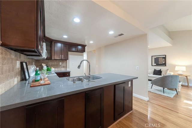 kitchen featuring dark brown cabinets, a sink, light wood-style floors, a peninsula, and visible vents