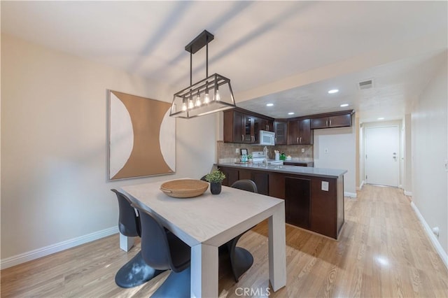 kitchen featuring dark brown cabinets, light wood-style floors, a peninsula, baseboards, and white microwave