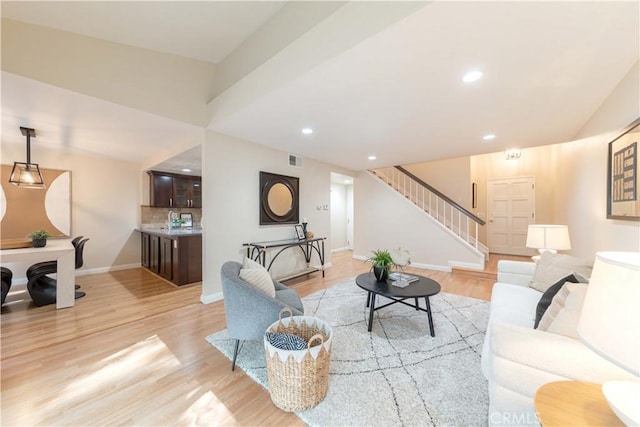 living room featuring stairs, baseboards, visible vents, and light wood-type flooring