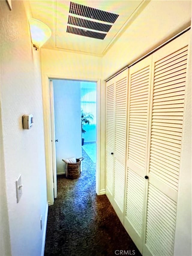 corridor featuring baseboards, dark colored carpet, and visible vents