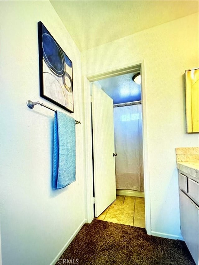 corridor featuring baseboards, tile patterned flooring, and carpet flooring