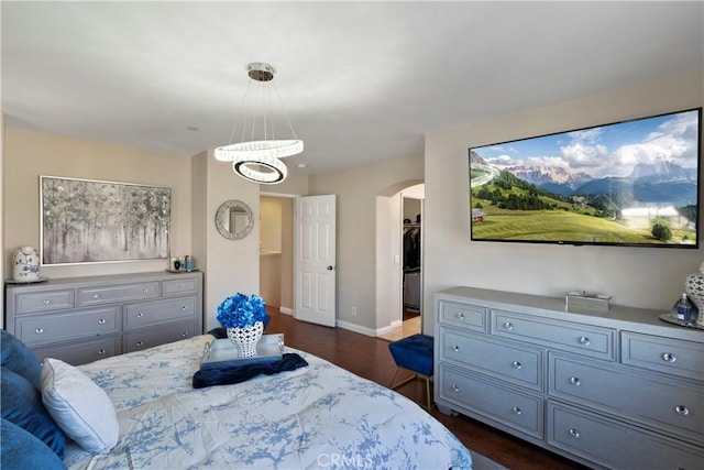 bedroom featuring arched walkways, baseboards, a spacious closet, an inviting chandelier, and dark wood-type flooring