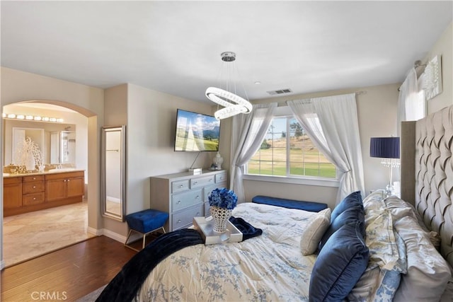bedroom with visible vents, arched walkways, baseboards, light wood-style floors, and ensuite bath