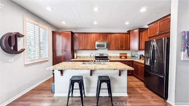 24939 Coral Canyon Rd, Corona, CA 92883 - kitchen featuring appliances with stainless steel finishes, a sink, light wood-style floors, an island with sink, and a breakfast bar area