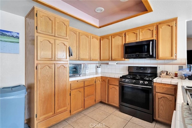 19804 Haida Rd, Apple Valley, CA 92307 - kitchen featuring tile countertops, a raised ceiling, backsplash, light tile patterned floors, and black gas range oven