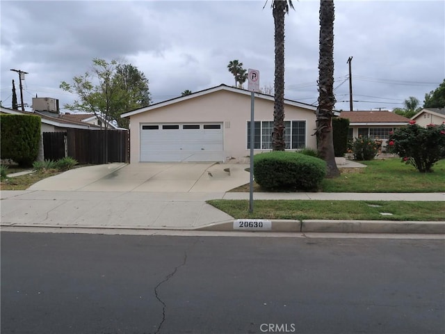 ranch-style home with a garage, fence, stucco siding, and driveway