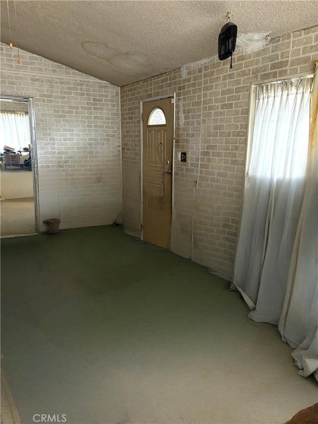 foyer entrance featuring brick wall, lofted ceiling, and plenty of natural light