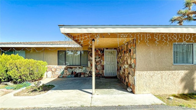 property entrance with a patio, stucco siding, and stone siding