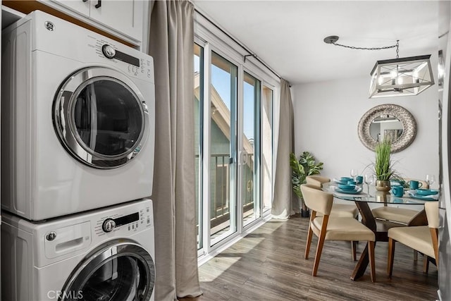laundry area featuring dark wood-type flooring, cabinet space, stacked washing maching and dryer, and a chandelier