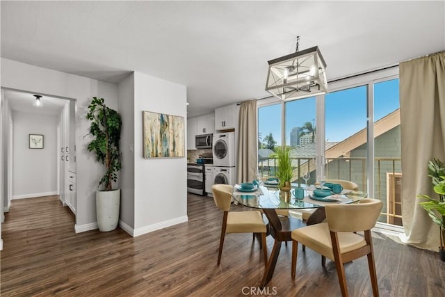 dining space with baseboards, stacked washer / drying machine, a chandelier, and dark wood-type flooring