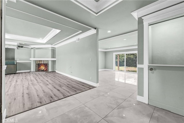 interior space with baseboards, ornamental molding, a lit fireplace, and a tray ceiling