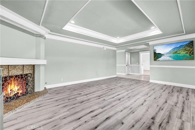 unfurnished living room with a raised ceiling, a premium fireplace, recessed lighting, wood finished floors, and ornamental molding