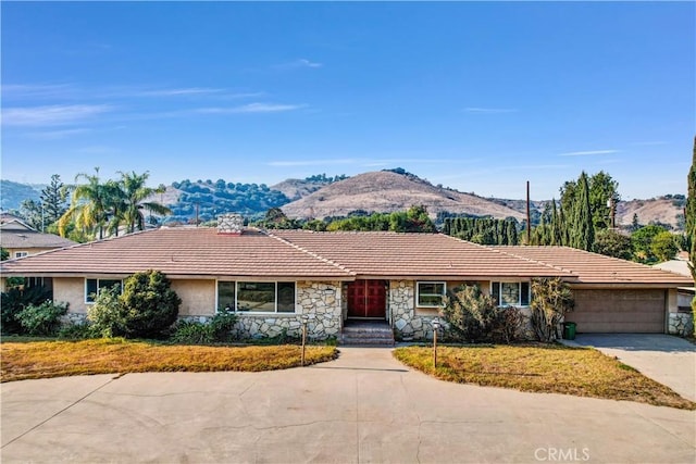 ranch-style house featuring a garage, stone siding, a tiled roof, a mountain view, and driveway