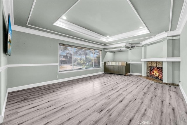 unfurnished living room featuring ornamental molding, wood finished floors, a lit fireplace, recessed lighting, and a tray ceiling