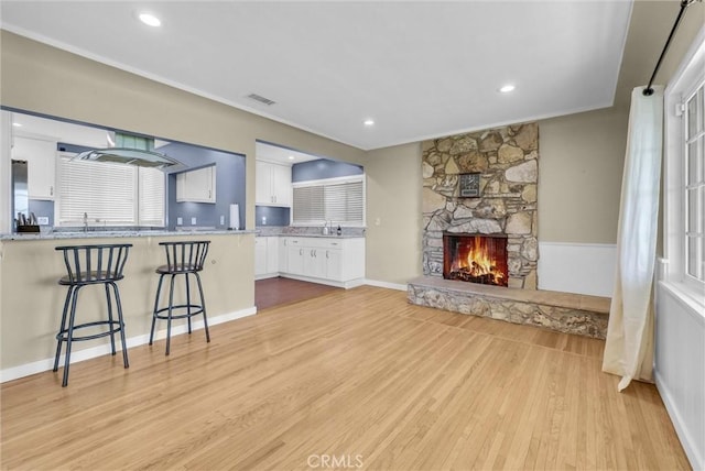 living area featuring recessed lighting, light wood finished floors, a stone fireplace, and visible vents